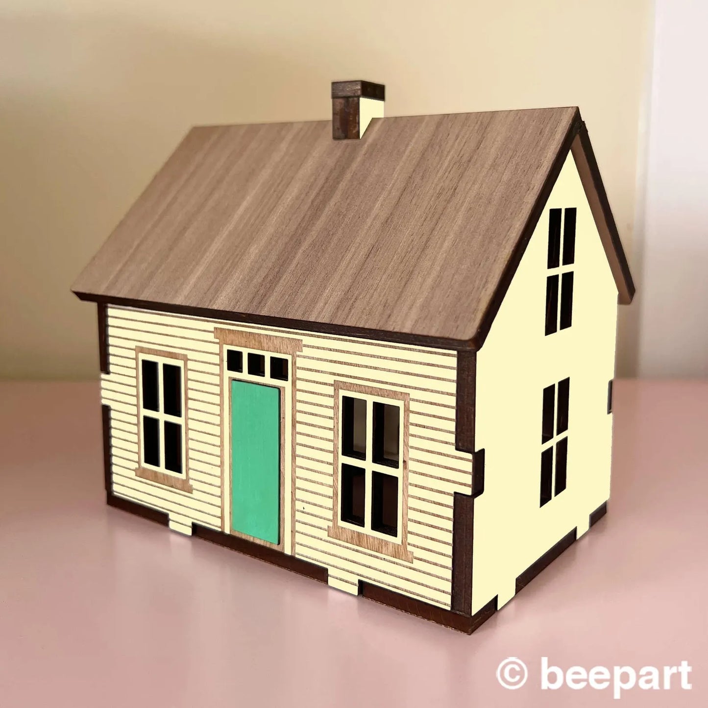 Model house with wooden roof and cream walls on a pink surface